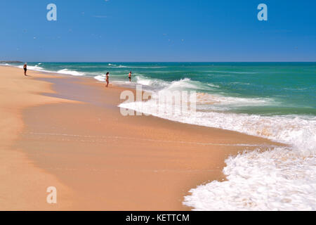 La gente gode di una giornata calda sulla spiaggia di sabbia con acqua verde e onde morbide Foto Stock