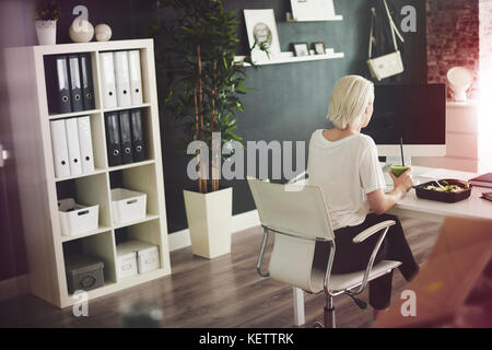 Imprenditrice di mangiare alla scrivania nel suo ufficio a casa Foto Stock