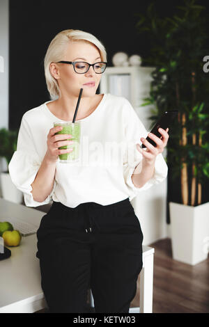 Donna con smoothie texting al lavoro Foto Stock