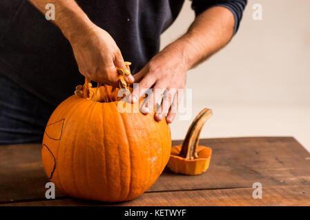 Mani maschio carving zucca tenendo fuori i semi Foto Stock