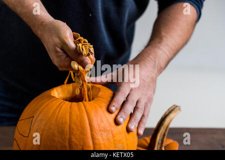 Mani maschio carving zucca tenendo fuori i semi Foto Stock