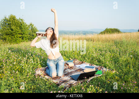 Ragazza piace ascoltare musica e leggere libri mentre si divertono sul campo in erba Foto Stock