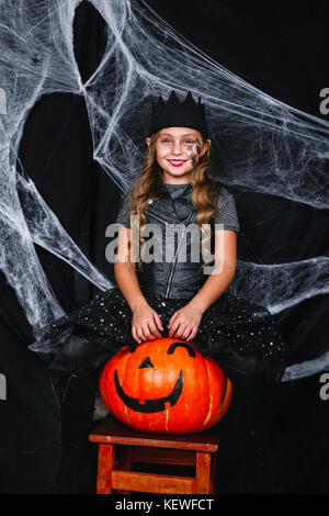 Carino piccolo ragazza in costume di halloween seduti sulla zucca sullo sfondo con una ragnatela Foto Stock