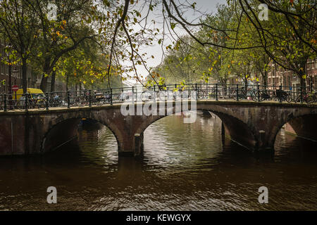 Autunno luce ricade su biciclette parcheggiate su un ponte sopra un canale di Amsterdam. Foto Stock