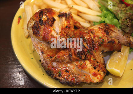Piastra di grigliate alla fiamma di pollo piccante con un pezzo di limone e insalata verde Foto Stock