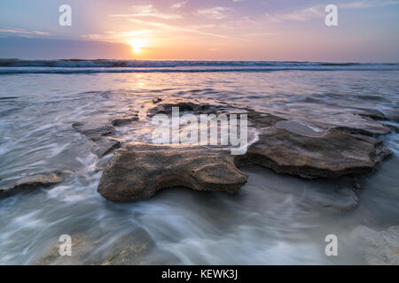 Sunrise al di sopra della marea turbinano intorno una coquina rock a Marineland Beach, Florida Foto Stock