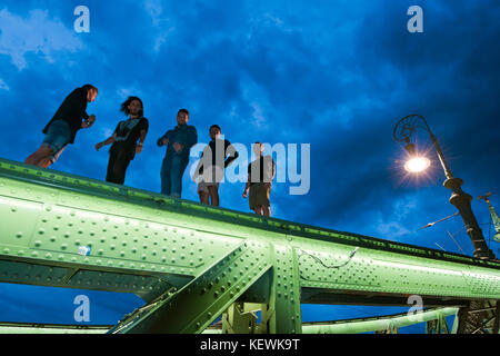 Vista orizzontale della gente che camminava sulle travi di Szabadság híd o Ponte della Libertà chiusa al traffico di notte a Budapest. Foto Stock