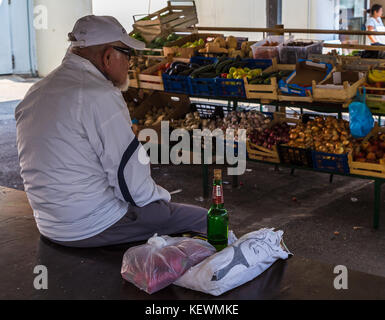 Titolare di una pensione o di una rendita si siede su una tabella vuota nel mercato di frutta e verdura della citta di Hvar con una bottiglia di birra. Foto Stock