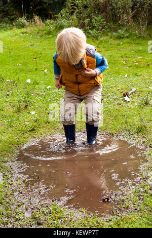 Ragazzo divertendosi schizzi nelle pozzanghere fangose Foto Stock