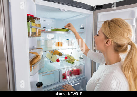 Close-up di giovane donna prendendo il cibo da mangiare da frigorifero Foto Stock