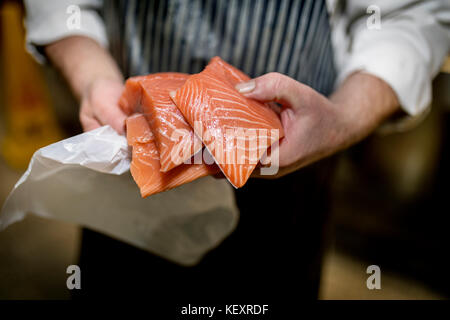 Close up di un pesce monger le mani tenendo tre filetti di filetti freschi Salmone su un mercato in stallo nello Yorkshire, Inghilterra Foto Stock