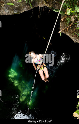 Femmina rappels turistica verso il basso la fune in Gran Cenote Maya, vicino al sito archeologico di Ek Balam in Valladolida, Yucatan, Messico Foto Stock