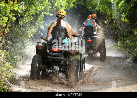 Vista posteriore di coppie guida quad bikes attraverso la strada sterrata pozzanghere in emozioni Parco nativo, Quintana Roo, Messico Foto Stock