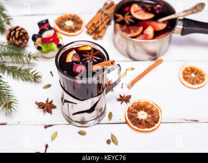 Vin brulé in un bicchiere con un ferro da stiro portabicchieri su un bianco sullo sfondo di legno Foto Stock