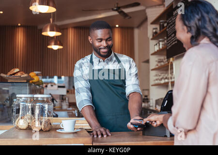 Sorridente barista utilizzando la tecnologia NFC per un cliente per il pagamento Foto Stock