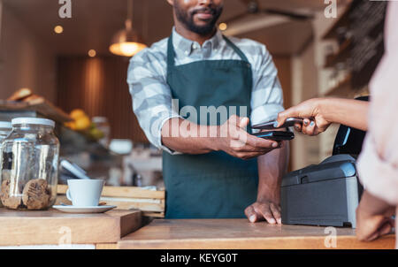 Il cliente utilizza la tecnologia NFC per pagare il suo cafe acquisto Foto Stock