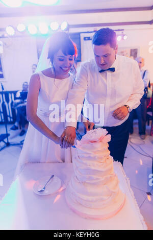 Felice sposa giovane è il taglio il loro primo pezzo di torta nuziale. Foto Stock