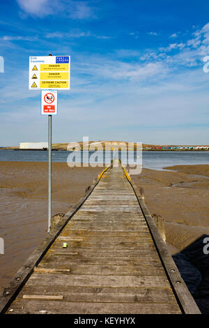 Un pontile in legno che si allunga nel fiume Tamigi con la bassa marea, sull'altro lato del fiume è Rainham discarica in Essex, Erith, London, Regno Unito Foto Stock