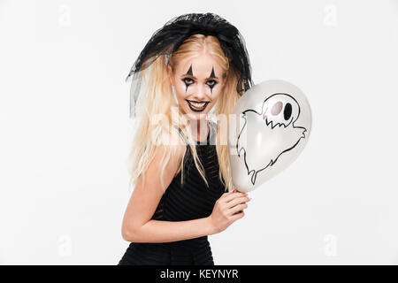 Crazy donna bionda vestita di nero vedova costume holding palloncino di halloween e sorridente isolate su sfondo bianco Foto Stock