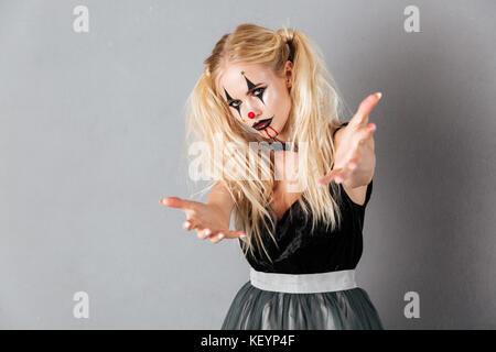 Giovane donna bionda in halloween make up si estende le sue mani e guardando la telecamera su uno sfondo grigio Foto Stock