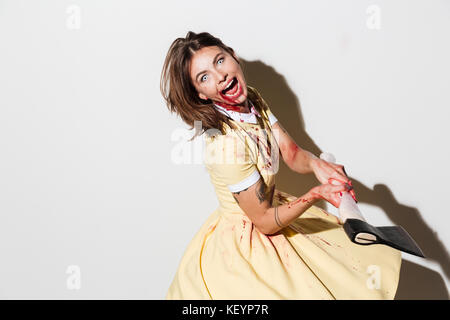 Vista laterale del pazzo urlando donna zombie che attacca con un'ascia su sfondo bianco Foto Stock