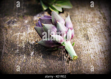 Carciofi viola sul rustico sfondo di legno Foto Stock