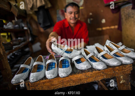 Un calzolaio di Salvadoran visualizza di nuovo reso coppie di ragazza silver glitter scarpe sul banco di lavoro in una scarpa rendendo il workshop in San salvador el salvado Foto Stock