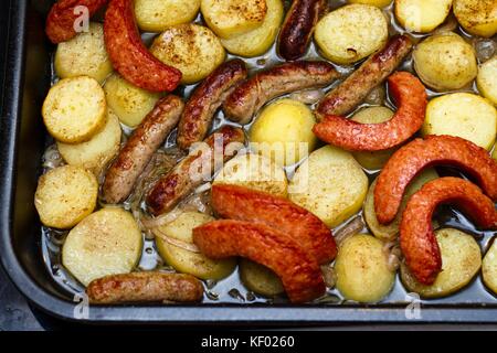 Diversi tipi di salsicce e patate arrosto essendo in nero la tostatura vassoio per un delizioso brunch caldo Foto Stock