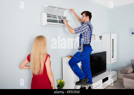 Donna che guarda la giovane maschio tecnico di manutenzione o riparazione di condizionatore d'aria di casa Foto Stock