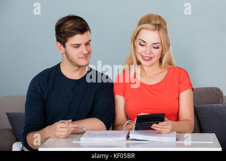 Giovane coppia sorridente calcolando Family Money Budget e tasse utilizzando Calcolatrice a casa Foto Stock