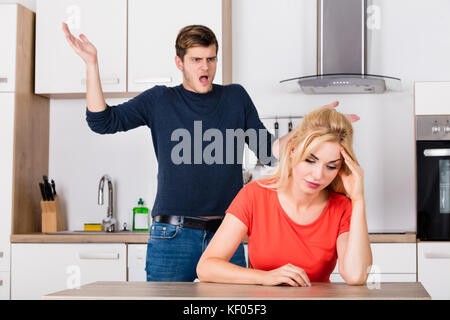 Uomo arrabbiato gridando alla sua moglie infelice depressa durante la disputa nella cucina a casa Foto Stock