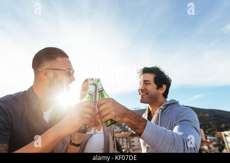 Un gruppo di uomini e donne birre di tostatura ad una festa sul tetto. Giovani amici appendere fuori a parte sul tetto e godersi un drink. Foto Stock
