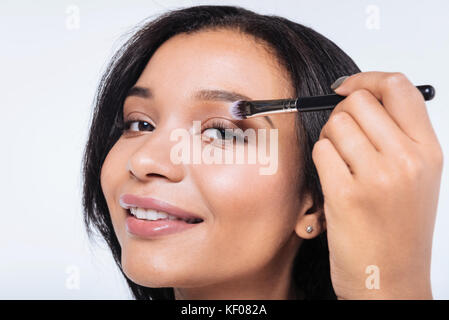 Close up di donna sorridente applicando eyeshadows Foto Stock