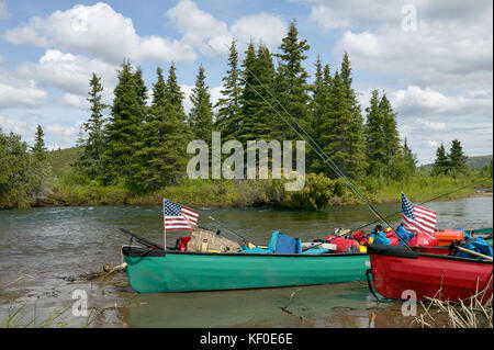 Due spiaggiata canoe con bandierine americane su un telecomando, scenic alaskan banca di fiume con una soleggiata cielo blu e lussureggiante foresta sullo sfondo. Foto Stock