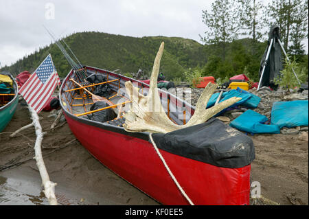 Canoe, uno con una bandiera americana e palchi, tirata su un alaskan banca del fiume accanto a un campeggio. Foto Stock