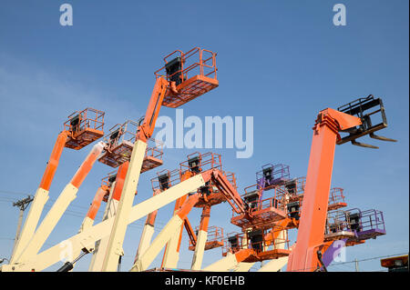 A basso angolo di visione di un arancio grande gruppo di piattaforma di lavoro aerea contro il cielo blu chiaro Foto Stock