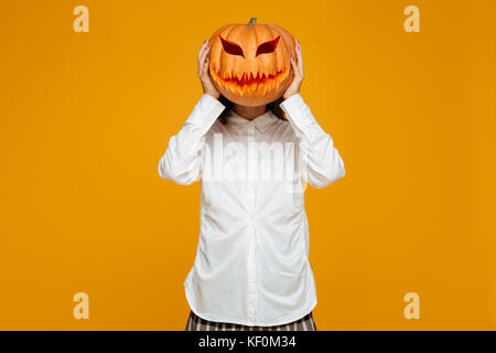 Funny teenage schoolgirl in uniforme tenendo la zucca di Halloween presso la sua testa isolate su sfondo arancione Foto Stock