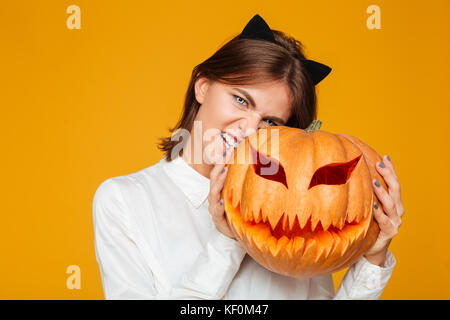 Immagine emotiva di giovane donna vestita di crazy cat costume di halloween su sfondo giallo con la zucca. Foto Stock