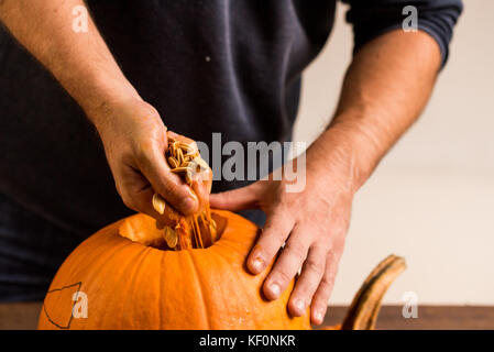 Mani maschio carving zucca tenendo fuori i semi Foto Stock