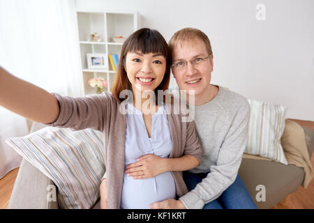 Donna incinta con il marito tenendo selfie a casa Foto Stock