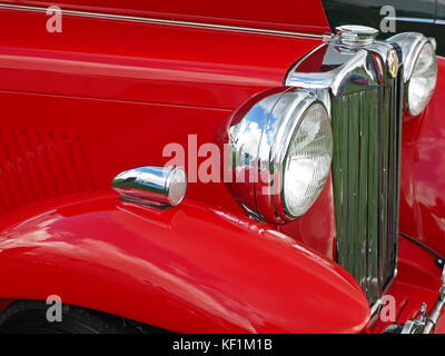 Dettaglio di un auto classica mostra finestrino laterale cromato,il faro e la griglia del radiatore e vernice rossa di MG roadster auto sportiva Foto Stock