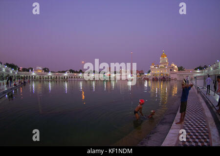 Delhi, India - 19 settembre 2017: persone non identificate swiming e camminare nei pressi del laghetto artificail, con una bella vista del famoso Gurdwara Sikh tempio dorato Harmandir Sahib si riflette nel laghetto artificiale, con uno splendido cielo viola in India Foto Stock