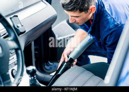 Giovane uomo utilizzando il vuoto per la pulizia della parte interna di una automobile Foto Stock