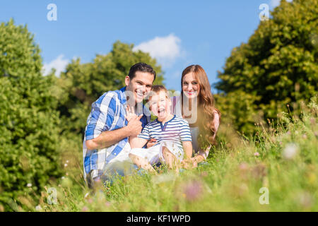 Famiglia seduta sul prato con bambino sventolare le mani Foto Stock