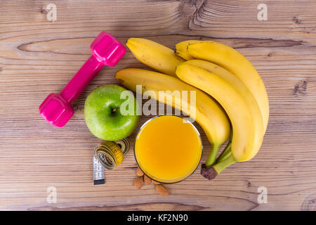 Close up vista dall'alto di frutti, banane, succo di arancia, succo di mela verde, nastro di misurazione, mandorla con un sano concetto di montare su sfondo di legno. Foto Stock