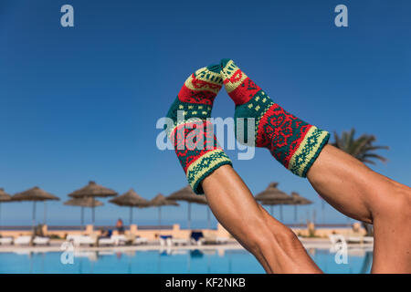 Calza di Natale su Palm tree a esotica spiaggia tropicale. il concetto di vacanza per capodanno carte. calzino di Natale su un soleggiato gambe di donne attraenti in retro Foto Stock