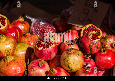 I semi di melograno sparkle in autunno sole quanto essi siedono impilati su un mercato in stallo a dividere il mercato verde. Foto Stock