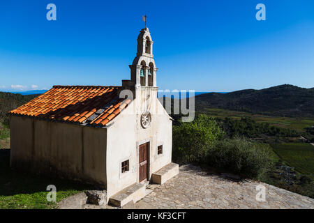 Una piccola chiesa sul bordo del villaggio rurale di smokvica sull isola di Korcula, raffigurato nella parte anteriore dei vigneti nella valle al di sotto e al di sotto di un blu Foto Stock
