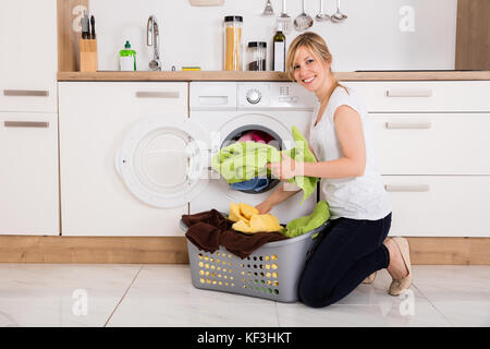 Giovane donna abiti di caricamento in macchina lavatrice in cucina Foto Stock