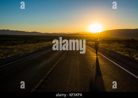 Donna che cammina verso il basso una lunga strada tortuosa al tramonto nella parte orientale del Nevada, Stati Uniti d'America Foto Stock